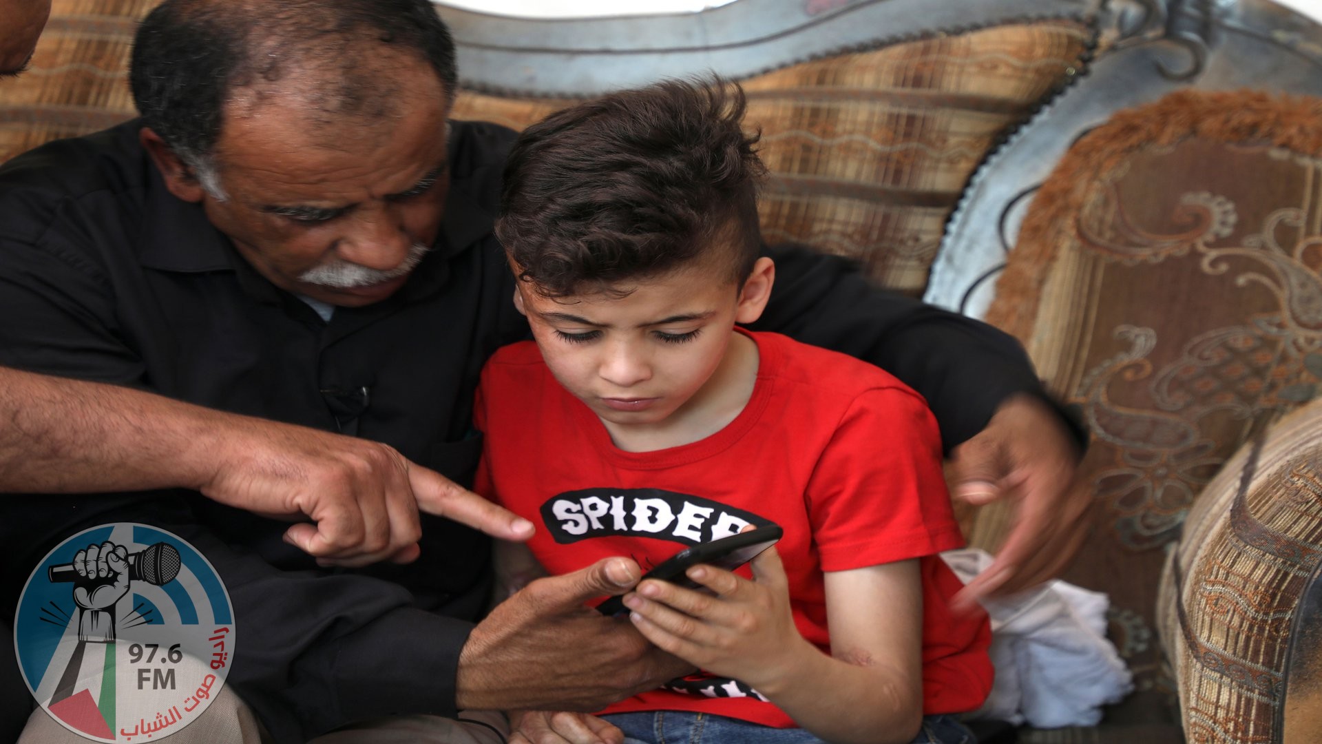 Hussein Dawabsha (L) sits with his grandson Ahmed, the survivor of the arson attack that killed his parents and 18-month-old brother, as they look at images on a phone at their home in the Israeli occupied West Bank village of Duma on May 18, 2020, after an Israeli court convicted a Jewish settler on three counts of murder over a 2015 arson attack. - Amiram Ben-Uliel, 25, from the West Bank settlement of Shilo, was also found guilty of two counts each of attempted murder and arson, along with conspiracy to commit a hate crime, a court statement said. (Photo by JAAFAR ASHTIYEH / AFP) (Photo by JAAFAR ASHTIYEH/AFP via Getty Images)